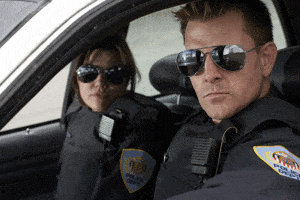 A man and lady cop sitting in a police car looking out a window.