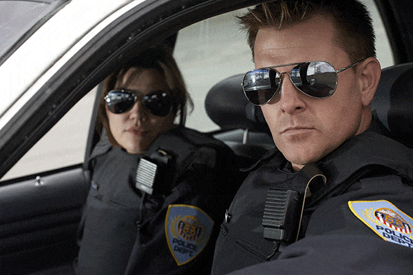 A man and lady cop sitting in a police car looking out a window.
