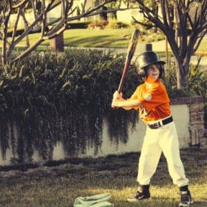 Little Kid wearing an orange baseball jersey golding a bat.