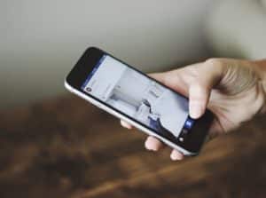 A hand holding a smart phone scrolling on social media.