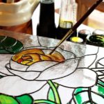 A small paint brush painting a piece of glass with etched flowers.