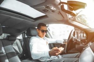 A man sitting in a car scrolling on his phone with an open sunroof.