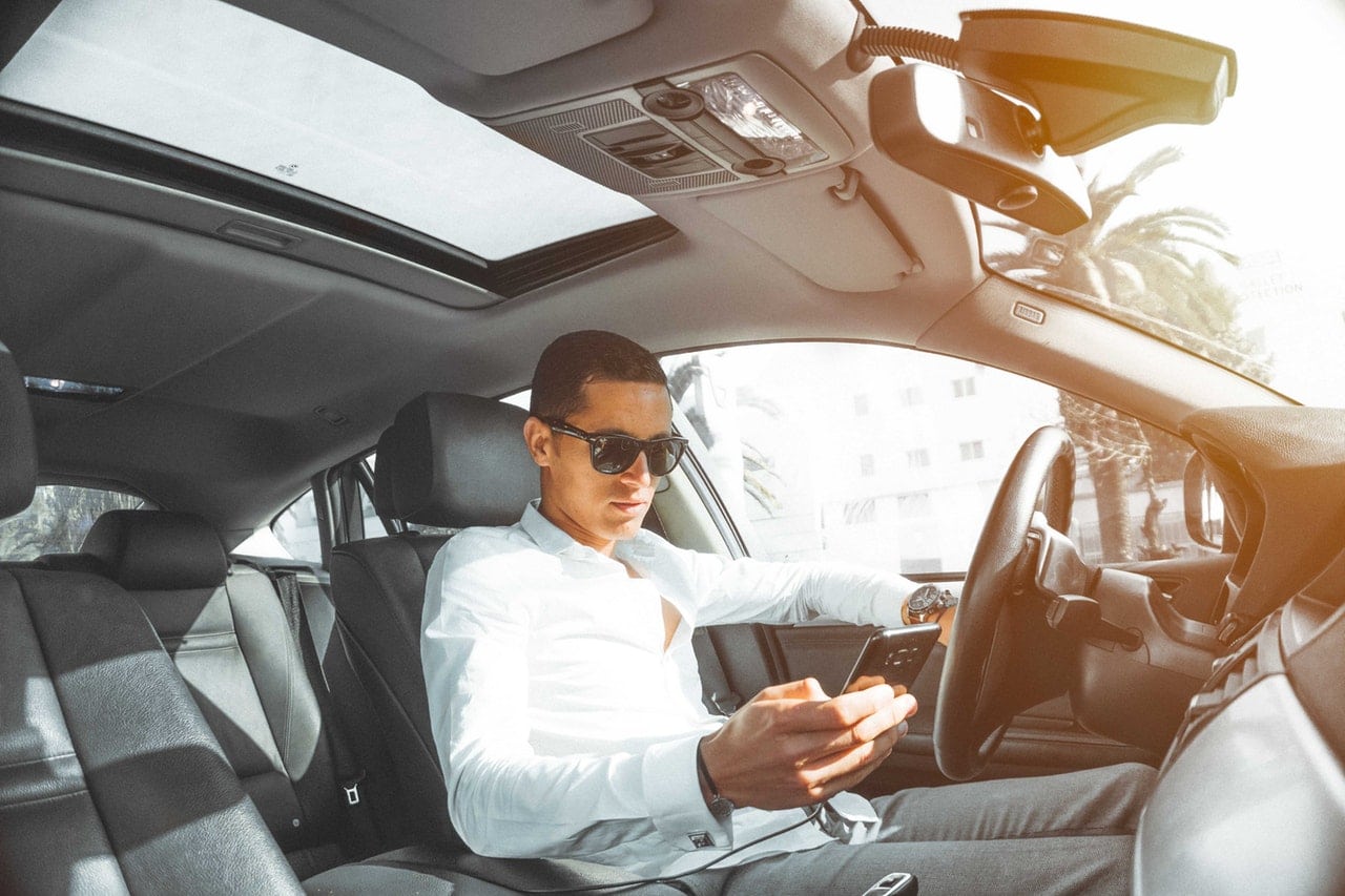 A man sitting in a car scrolling on his phone with an open sunroof.