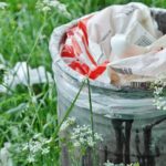 A trash can filled in the middle of tall green grasses.
