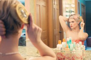 A women with short blonde hair looking at herself in the mirror as she brushes her hair.