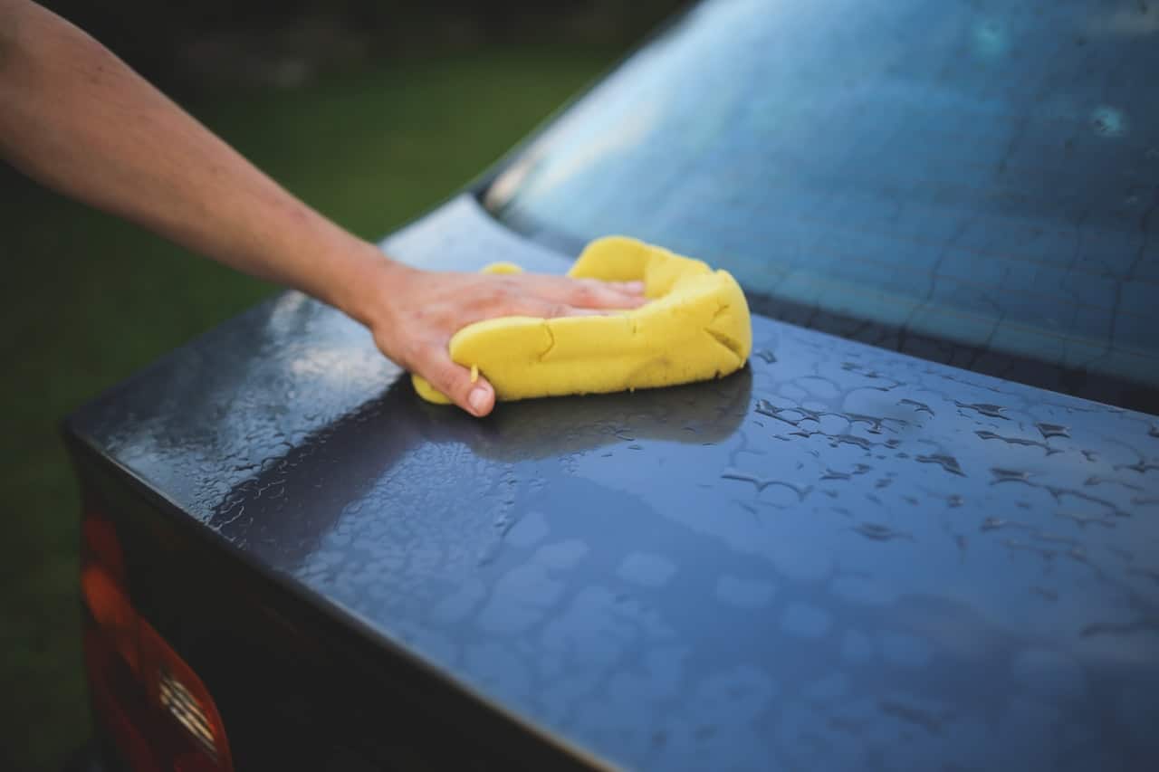 A hand using a yellow sponge to clean the back of a car.