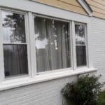 A white picture window from the exterior of a white brick home.
