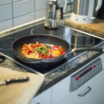 A sliver pan sits on a glass stove top filled with cut up yellow and red peppers.