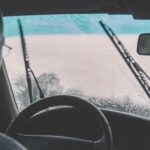 A man sits in the driver seat of a car with his windshield wipers on.