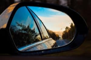 A reflection in a side car window. It is reflecting the side of the car, along with a blue cloud covered sky and road.