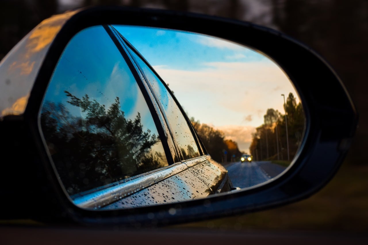 A reflection in a side car window. It is reflecting the side of the car, along with a blue cloud covered sky and road.