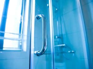 A closeup of a glass shower door's silver handle.