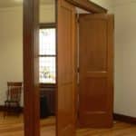 Three wooden trim-fold doors are opening leading to two different rooms.