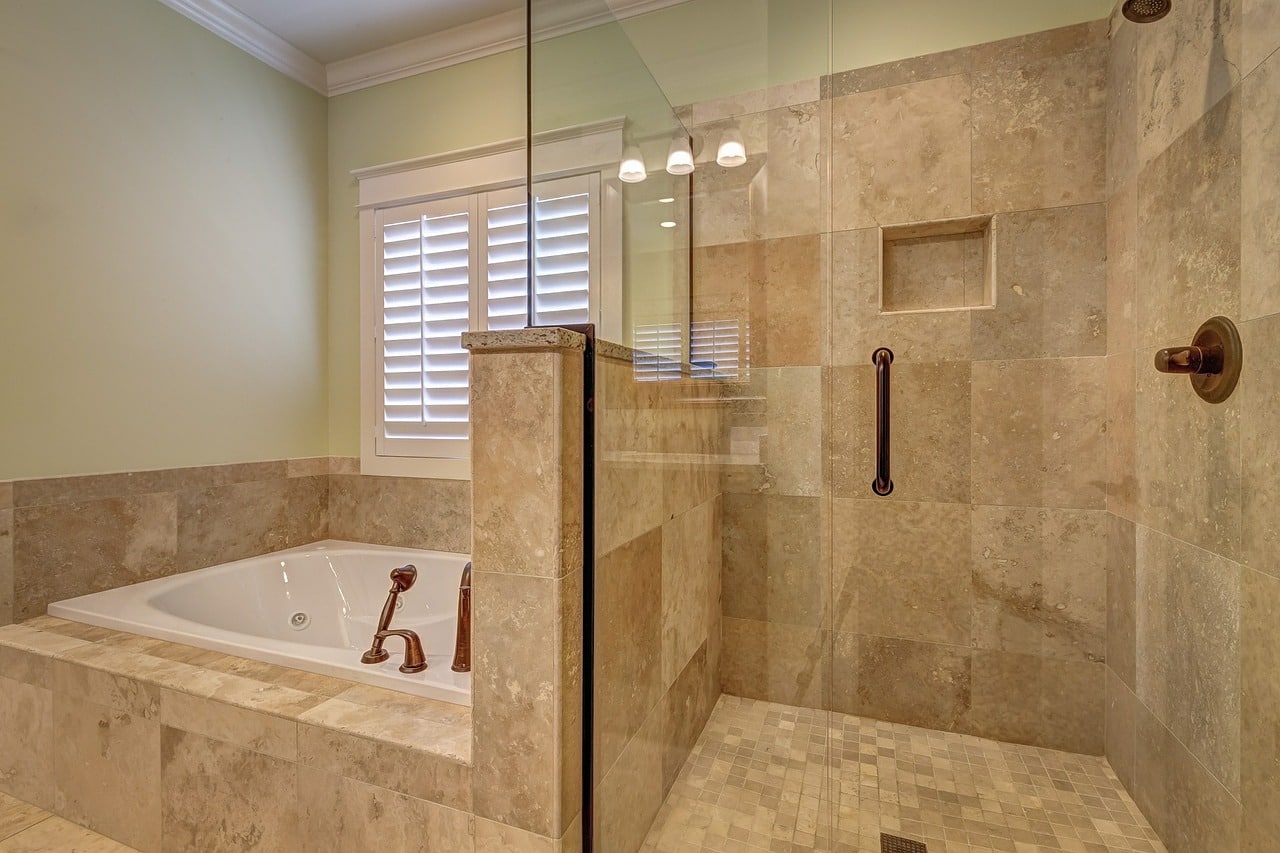 An open tiled shower with a glass door, sits next to the bathtub.