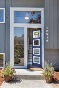 Blue front door with four horizontal windows is slightly open on a gray house.