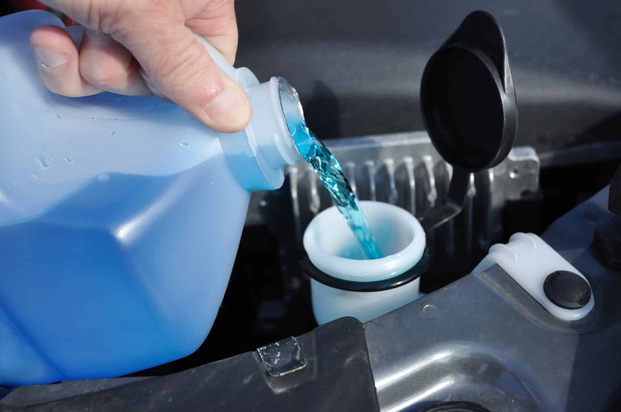 A hand pours blue windshield wiper fluid into the car.
