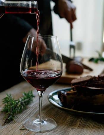 bordeux red wine glass being filled as it sits on a wooden table