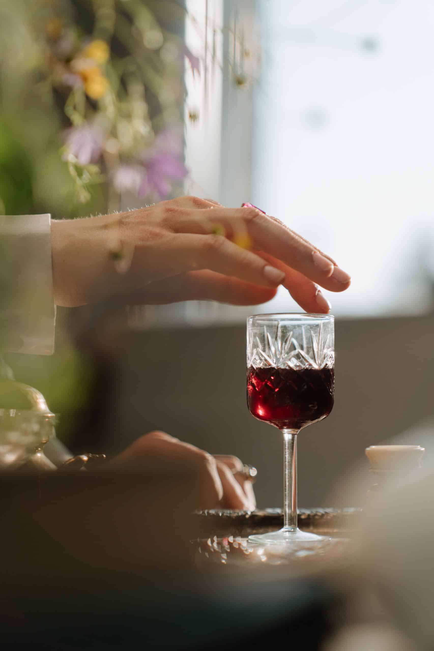 crystal wine glass sitting on a table with a hand touching the glass lip.