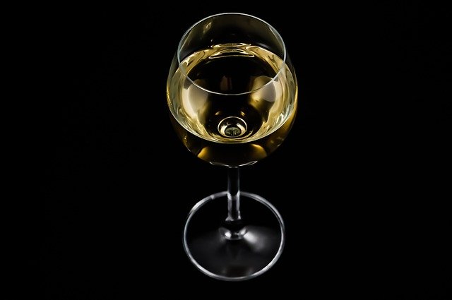 thin wine glass sits on a black background with white wine in it