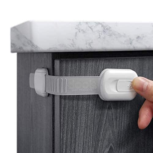 White child safely locks latches against a cabin side and on a cabinet door to keep from opening. A thumb shows the lock is a button on the from of the strap lock.